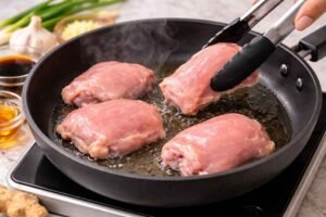 Chicken thighs cooking in skillet for cherry blossom chicken recipe