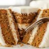 Moist carrot cake slice with cream cheese frosting and fork cutting into soft layers