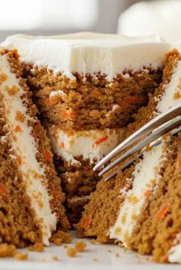 Moist carrot cake slice with cream cheese frosting and fork cutting into soft layers