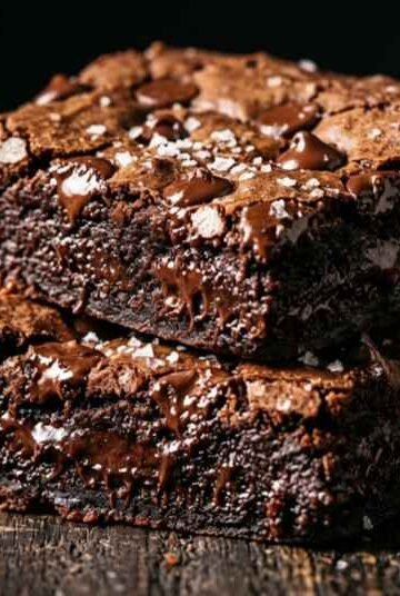 Fudgy sweet potato brownies stacked on dark parchment paper with melted chocolate chips and flaky sea salt