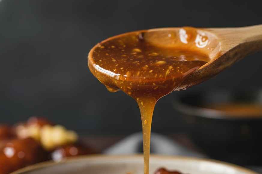 Thick glossy Wingstop Hawaiian sauce dripping off a wooden spoon showing restaurant-quality texture