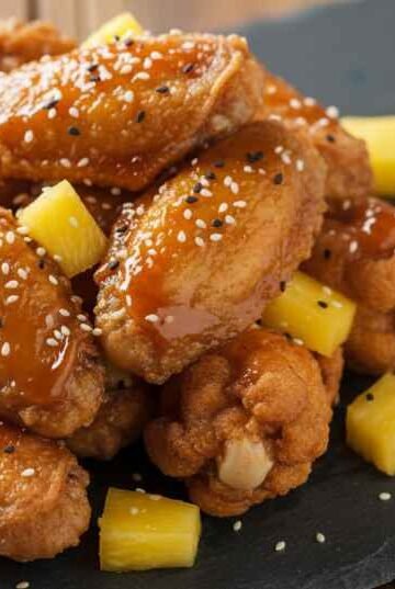 Crispy chicken wings coated in homemade Wingstop Hawaiian sauce recipe served on a slate board with pineapple garnish