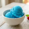 Two scoops of homemade blue raspberry ice cream in a white bowl showing vivid electric blue color and creamy no-churn texture