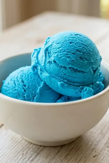 Two scoops of homemade blue raspberry ice cream in a white bowl showing vivid electric blue color and creamy no-churn texture
