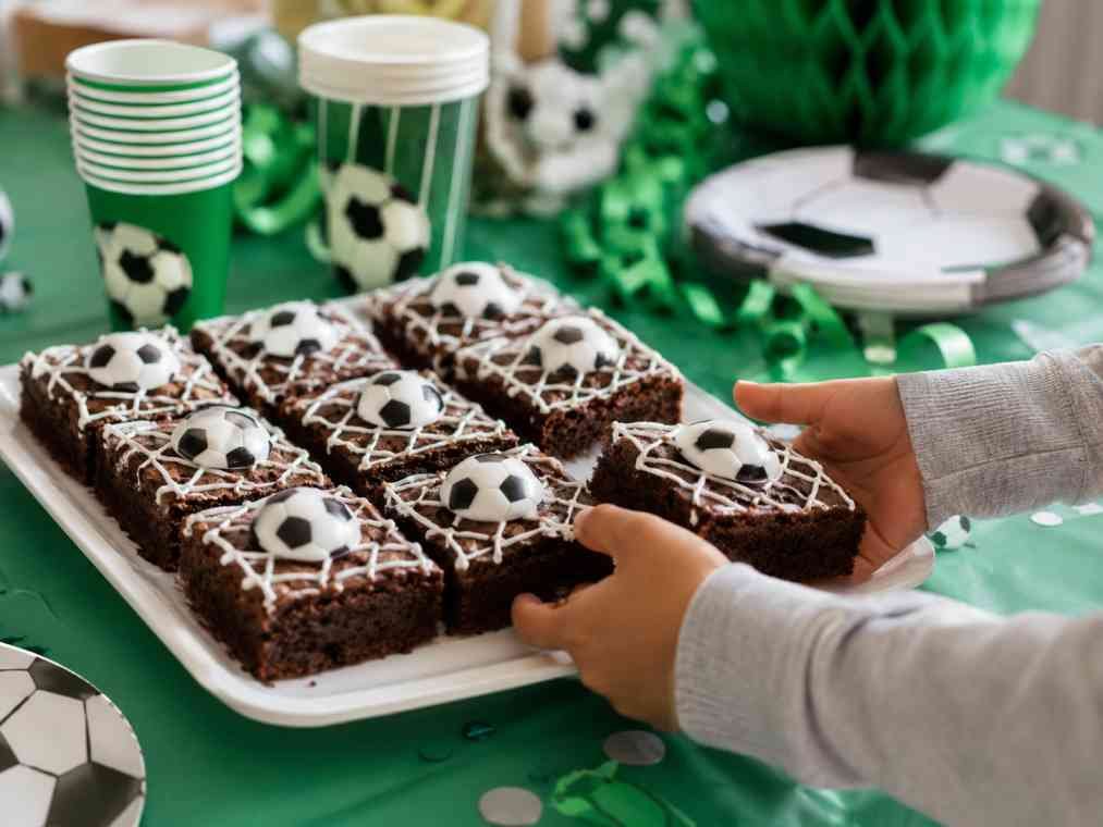 Homemade soccer brownies decorated with white icing and soccer ball patterns on a colorful kids' party table