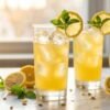 Two tall glasses of homemade Panera charged lemonade recipe with ice, fresh lemon wheels, and mint sprigs on a white marble surface.